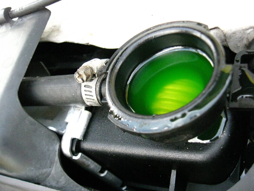 Bright green engine coolant filling an open reservoir under a car bonnet